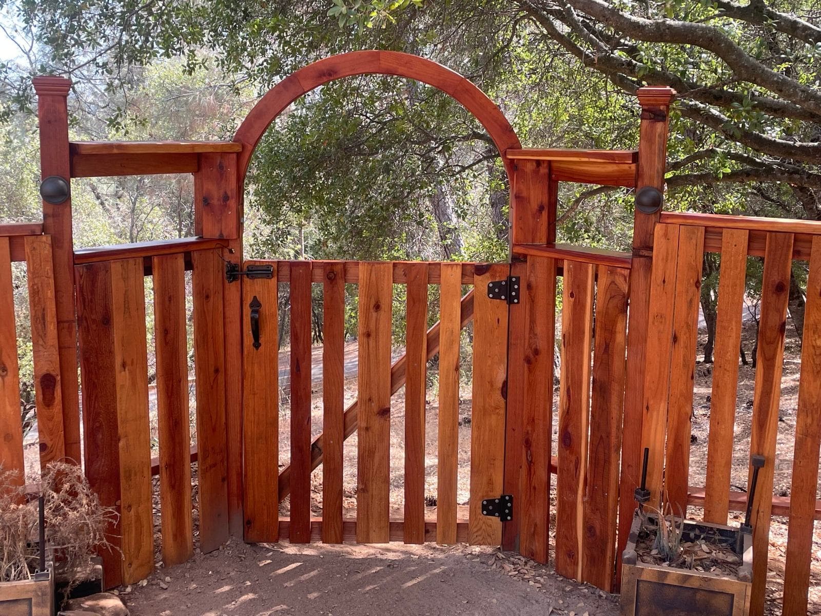 Custom Berco redwood archway gate with forged iron hardware and integrated low-voltage post lighting, under an oak canopy
